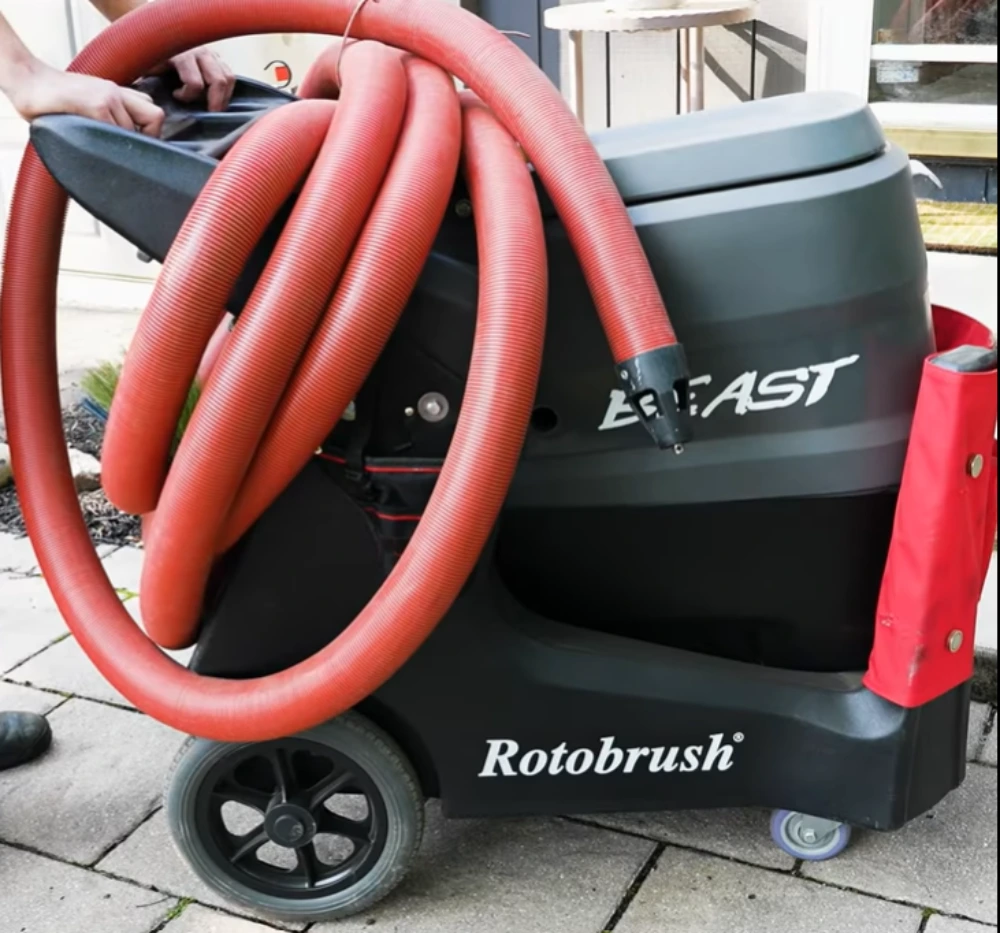 Rotary brush and negative-air vacuum hose cleaning debris from inside a residential air duct